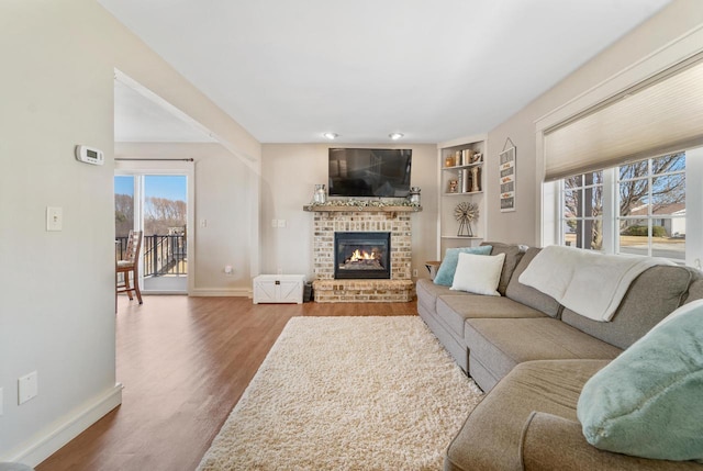 living area featuring a brick fireplace, built in features, wood finished floors, and baseboards