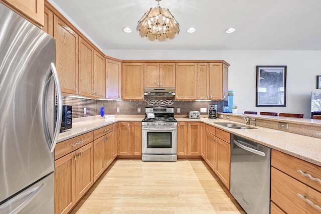 kitchen featuring under cabinet range hood, a sink, stainless steel appliances, light wood-style floors, and an inviting chandelier