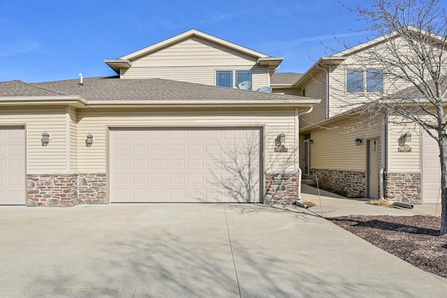 view of front of house with concrete driveway, a garage, stone siding, and roof with shingles