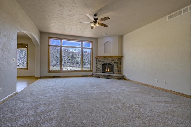 unfurnished living room featuring visible vents, carpet floors, a stone fireplace, and ceiling fan