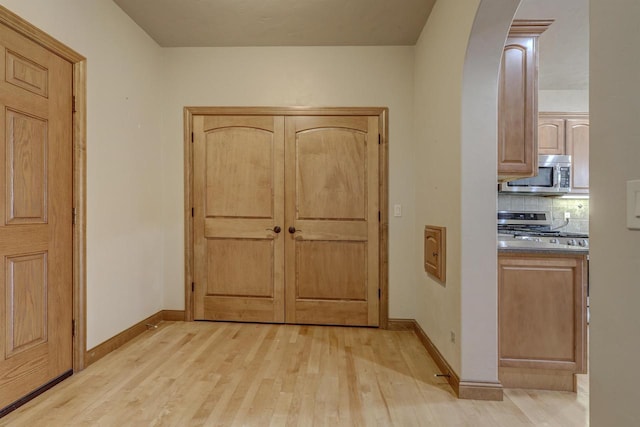 entrance foyer with light wood-style floors, arched walkways, and baseboards