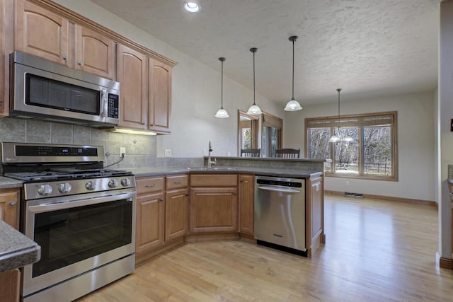 kitchen with a peninsula, a sink, stainless steel appliances, light wood-style floors, and backsplash