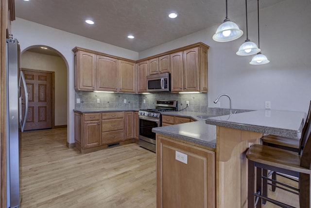 kitchen featuring a kitchen bar, appliances with stainless steel finishes, a peninsula, arched walkways, and a sink