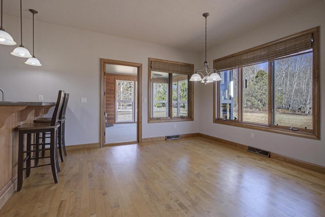 unfurnished dining area with light wood-type flooring, visible vents, baseboards, and a chandelier