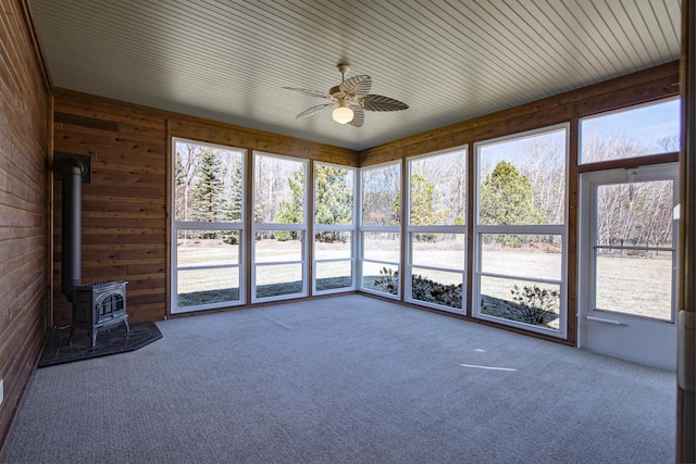 unfurnished sunroom featuring a wealth of natural light, a wood stove, and a ceiling fan