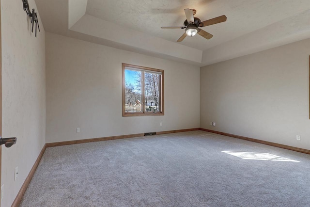 empty room featuring baseboards, a tray ceiling, carpet floors, and visible vents