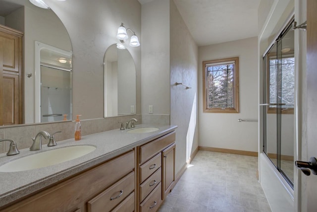 full bathroom featuring a sink, baseboards, combined bath / shower with glass door, and double vanity