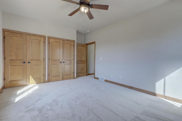 unfurnished bedroom with visible vents, multiple closets, a ceiling fan, carpet, and baseboards