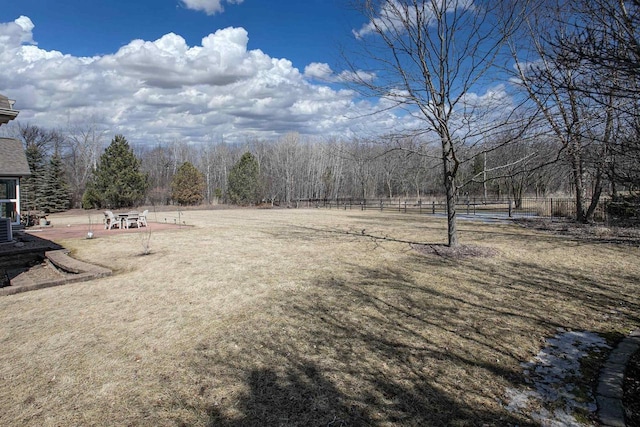 view of yard featuring central AC unit, a view of trees, and fence