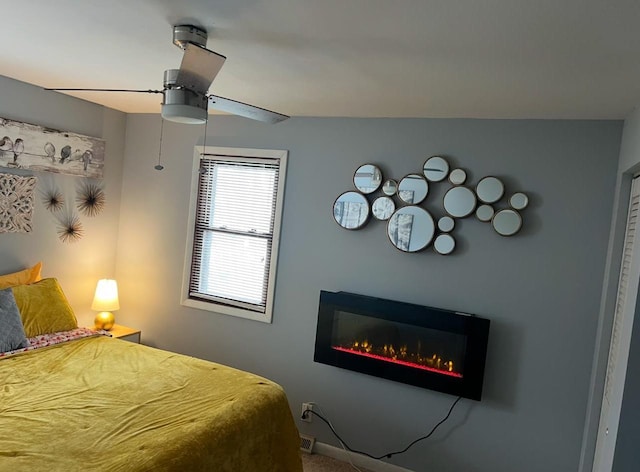 bedroom featuring a glass covered fireplace and a ceiling fan