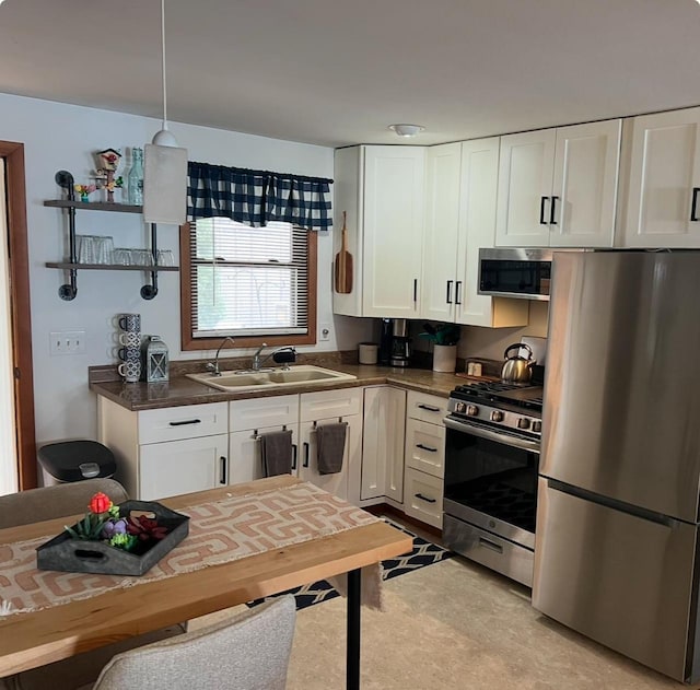 kitchen with a sink, decorative light fixtures, dark countertops, appliances with stainless steel finishes, and white cabinets