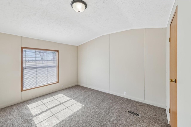 carpeted spare room featuring visible vents, a textured ceiling, and lofted ceiling