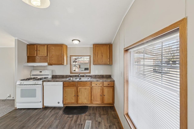 kitchen with a sink, dark countertops, dark wood-style floors, white appliances, and brown cabinetry