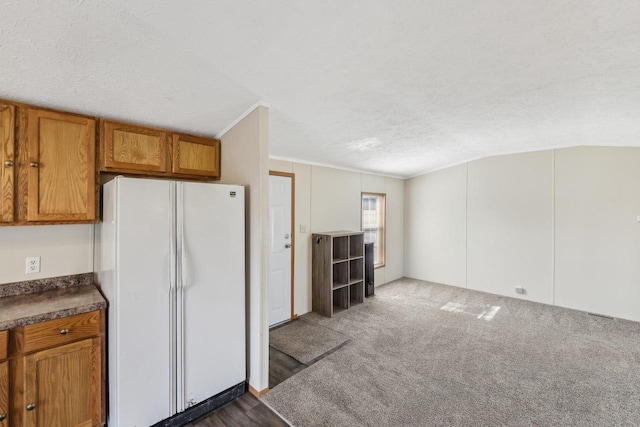 kitchen with brown cabinets, a textured ceiling, freestanding refrigerator, dark colored carpet, and lofted ceiling