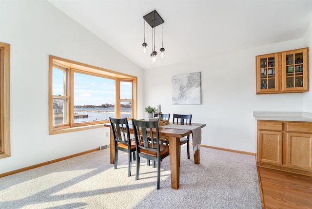 dining area with baseboards, lofted ceiling, visible vents, and a water view