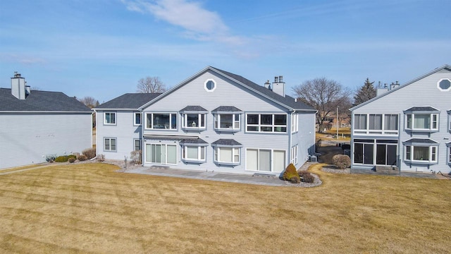 rear view of house with a lawn, a chimney, a patio, and a sunroom