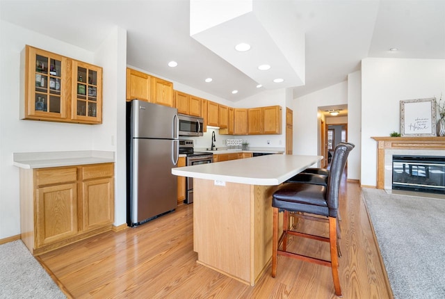 kitchen with a kitchen bar, stainless steel appliances, light countertops, glass insert cabinets, and vaulted ceiling