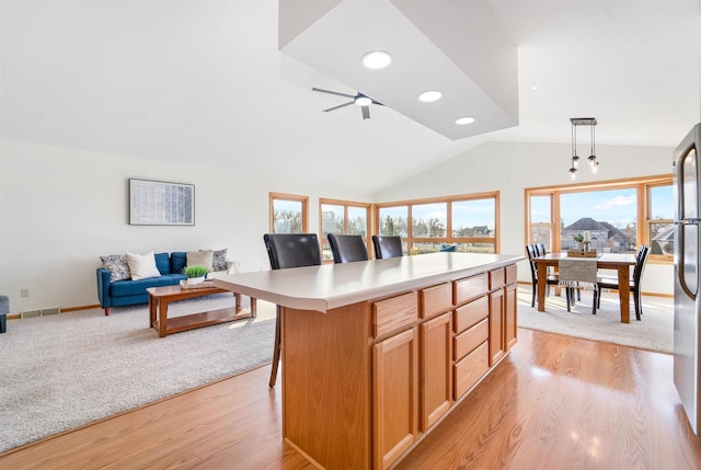 kitchen with visible vents, open floor plan, a breakfast bar area, light countertops, and vaulted ceiling