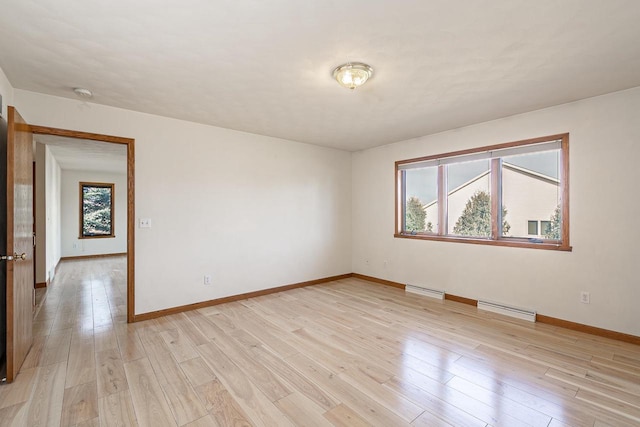 unfurnished room featuring a baseboard heating unit, light wood-style flooring, baseboards, and a wealth of natural light