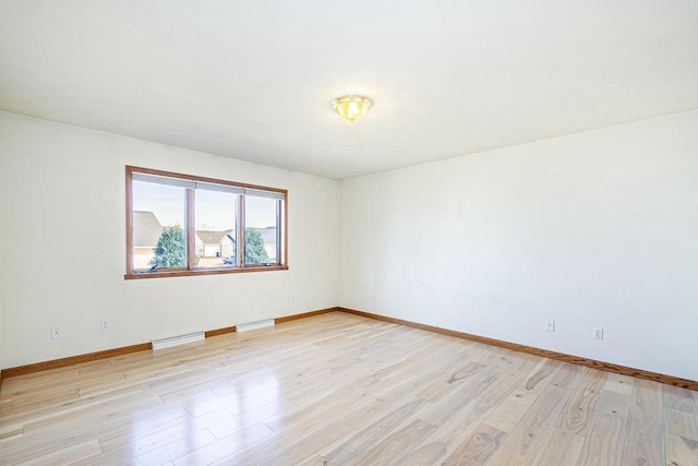 empty room featuring light wood-style flooring, baseboards, and baseboard heating