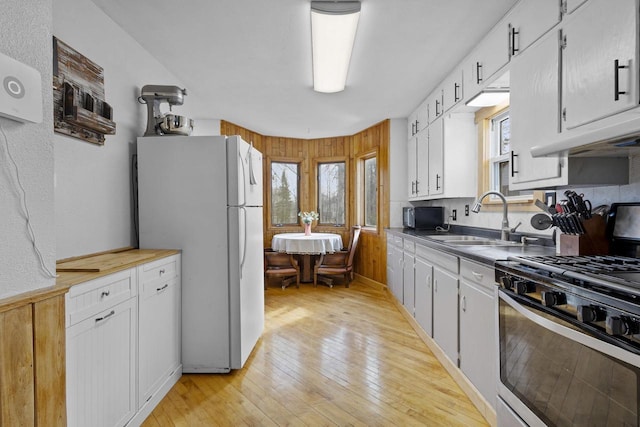 kitchen featuring a sink, white cabinetry, freestanding refrigerator, light wood finished floors, and stainless steel range with gas stovetop