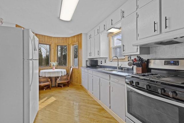 kitchen featuring under cabinet range hood, stainless steel range with gas stovetop, freestanding refrigerator, white cabinetry, and a sink