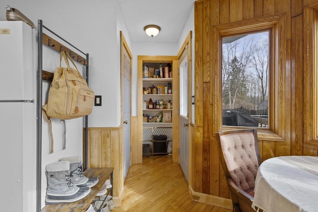 hallway with wooden walls, built in shelves, light wood-style flooring, and wainscoting