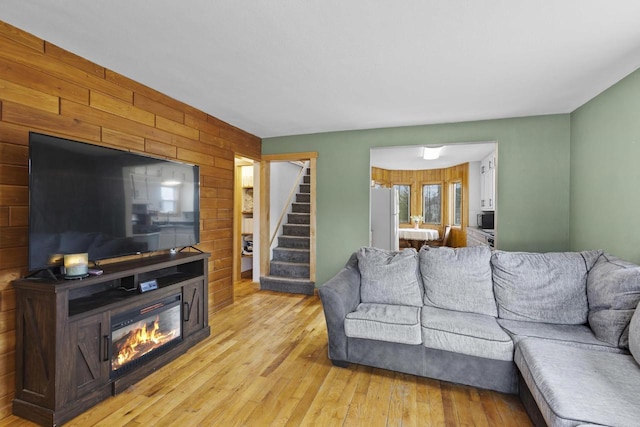 living room with a glass covered fireplace, stairway, wooden walls, and light wood-style floors