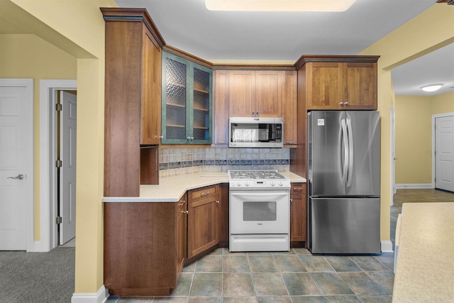 kitchen with tasteful backsplash, glass insert cabinets, light countertops, brown cabinets, and appliances with stainless steel finishes