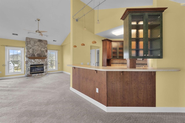 kitchen featuring glass insert cabinets, carpet floors, a stone fireplace, high vaulted ceiling, and a ceiling fan