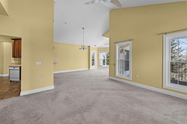 spare room featuring carpet flooring, ceiling fan with notable chandelier, high vaulted ceiling, and baseboards