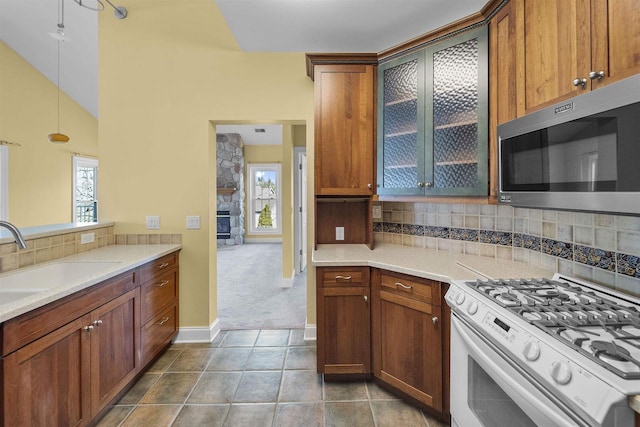 kitchen with white gas stove, a sink, stainless steel microwave, tasteful backsplash, and vaulted ceiling