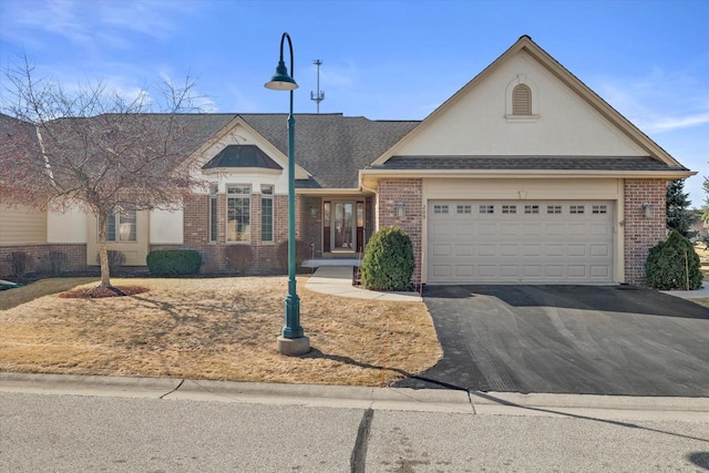 view of front of home with stucco siding, a shingled roof, a garage, aphalt driveway, and brick siding