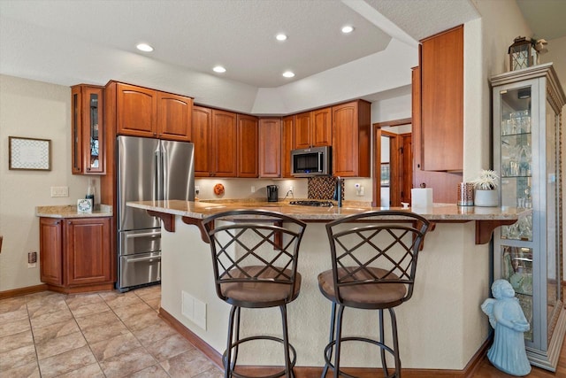 kitchen with a kitchen bar, a peninsula, glass insert cabinets, and appliances with stainless steel finishes