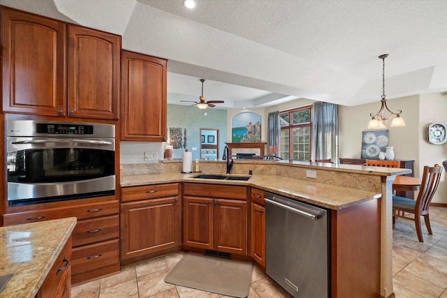 kitchen featuring a tray ceiling, a peninsula, a fireplace, stainless steel appliances, and a sink