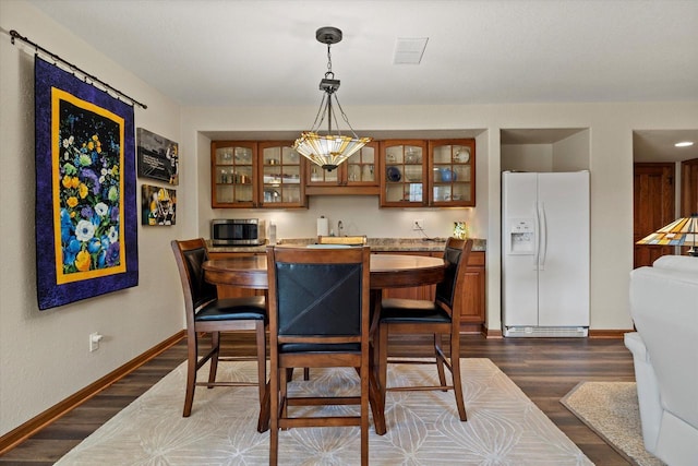 dining space with indoor wet bar, dark wood-type flooring, visible vents, and baseboards