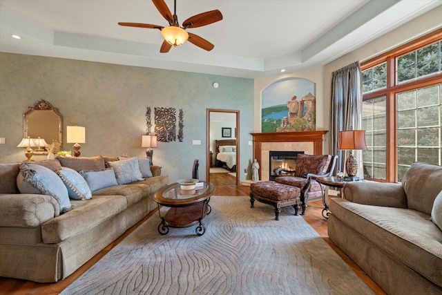 living room featuring recessed lighting, a tile fireplace, wood finished floors, a raised ceiling, and a ceiling fan