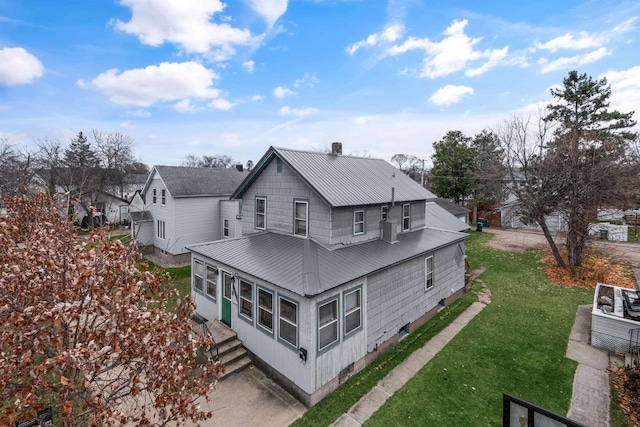 rear view of property with a chimney, a lawn, and metal roof