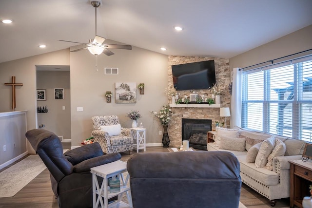 living room with wood finished floors, a ceiling fan, visible vents, lofted ceiling, and a stone fireplace