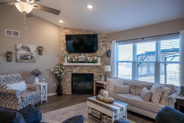 living room with a ceiling fan, wood finished floors, visible vents, a stone fireplace, and vaulted ceiling