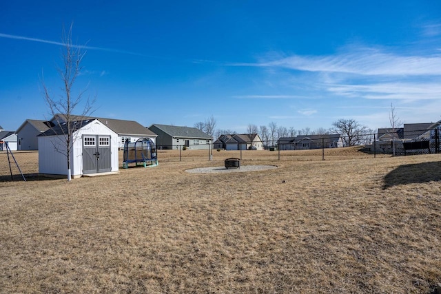 view of yard with an outdoor structure, a trampoline, fence, and a shed