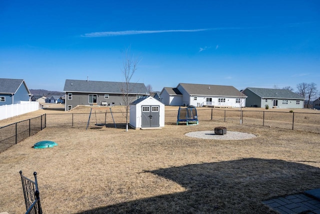 view of yard with a fire pit, a trampoline, a residential view, a fenced backyard, and an outbuilding