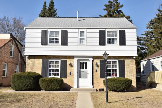 colonial-style house featuring brick siding, roof with shingles, and a front yard