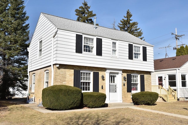 colonial inspired home featuring brick siding, a front lawn, and roof with shingles