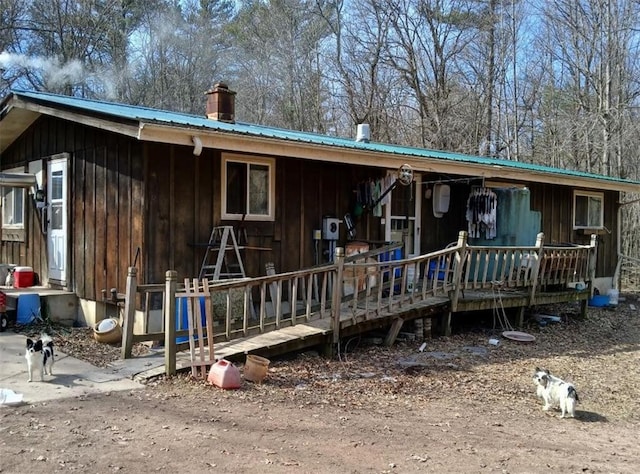 back of house with metal roof, board and batten siding, a chimney, and a porch