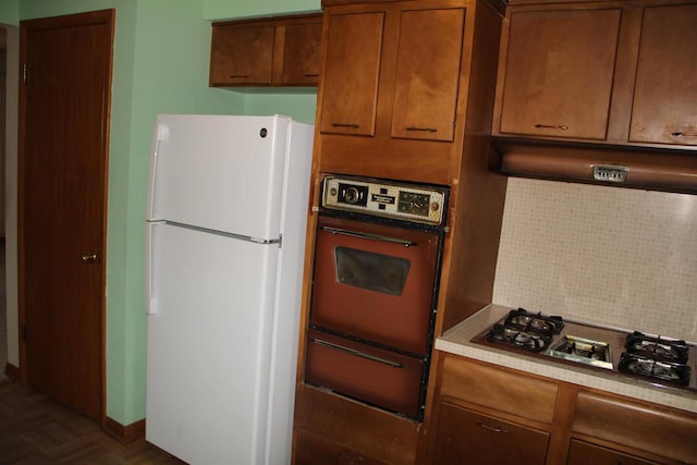 kitchen with oven, a warming drawer, under cabinet range hood, gas cooktop, and freestanding refrigerator