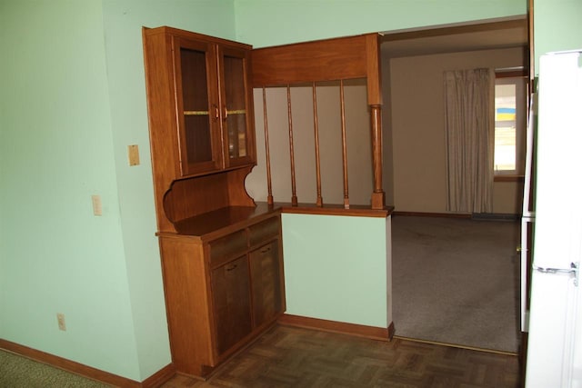 kitchen with glass insert cabinets, baseboards, brown cabinets, freestanding refrigerator, and dark colored carpet