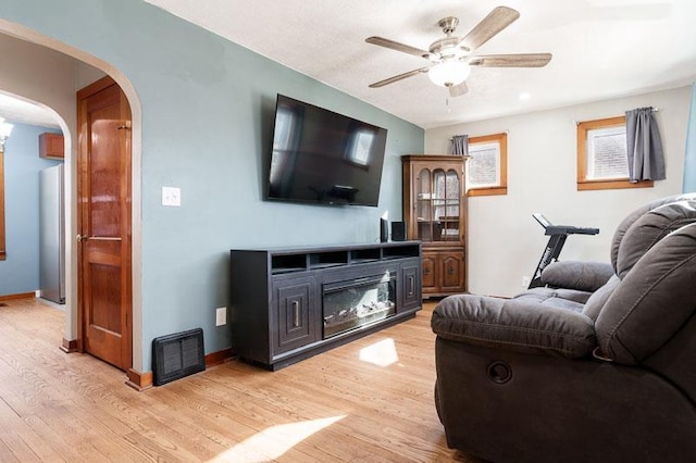 living room featuring a ceiling fan, light wood-style floors, arched walkways, and baseboards