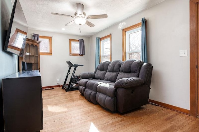 living room with light wood-style flooring, a textured ceiling, baseboards, and a ceiling fan