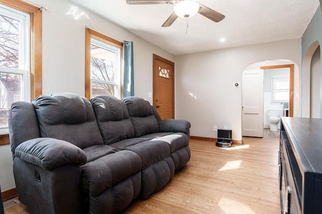 living room featuring light wood-type flooring, arched walkways, baseboards, and a ceiling fan